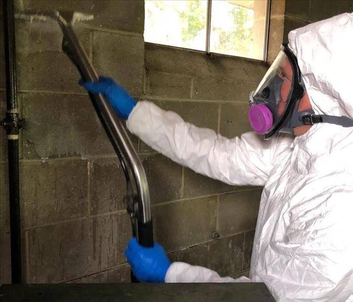 Man in PPE cleaning residue off of a brick wall. 